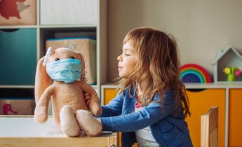 Toddler girl playing with rabbit soft toy in the medicine mask